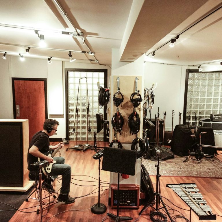 <img source='pic.gif' alt='Client recording guitar in a spacious recording studio filled with equipment.' />.